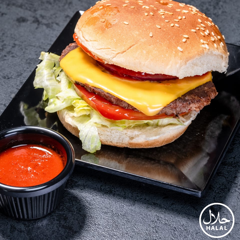 A Zaytoun Halal Grill cheeseburger with lettuce, tomato, and a side of red sauce.