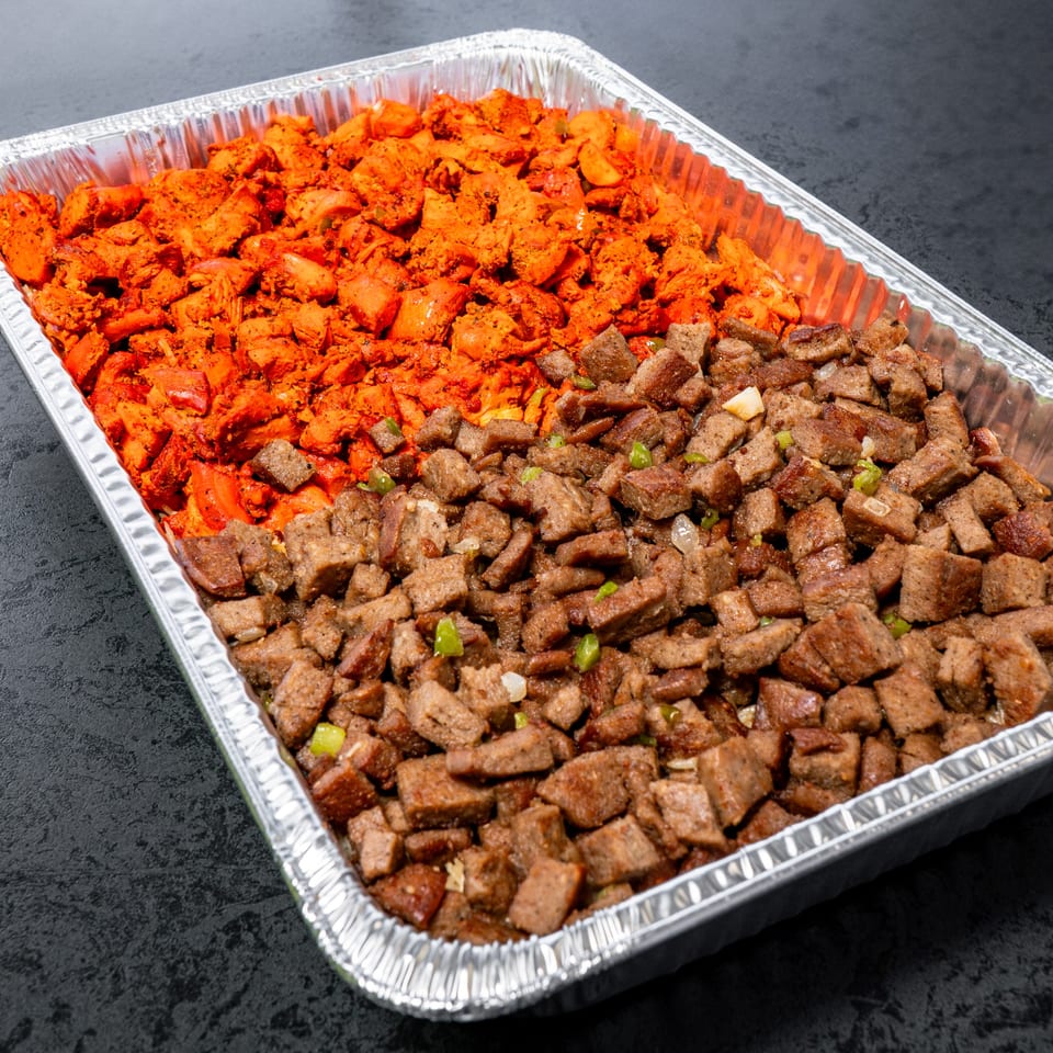 A catering tray with two sections of diced meat: red chicken on the left and brown beef on the right.