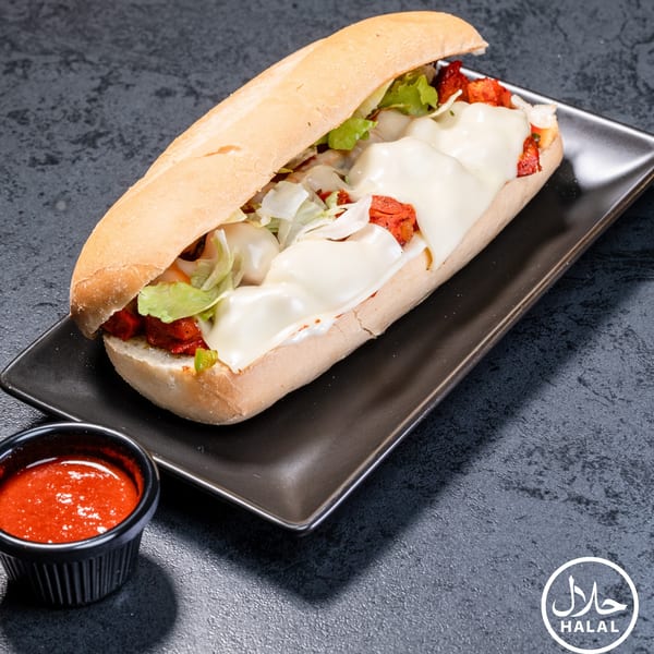 A Zaytoun Halal Grill chicken sub with melted cheese, lettuce, and red sauce on a dark plate.