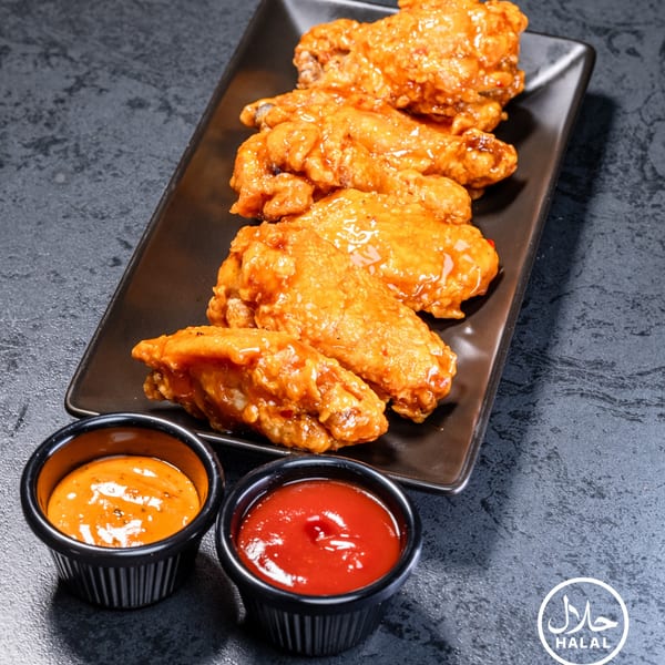 Zaytoun Halal Grill's glazed chicken wings on a black plate with two dipping sauces.