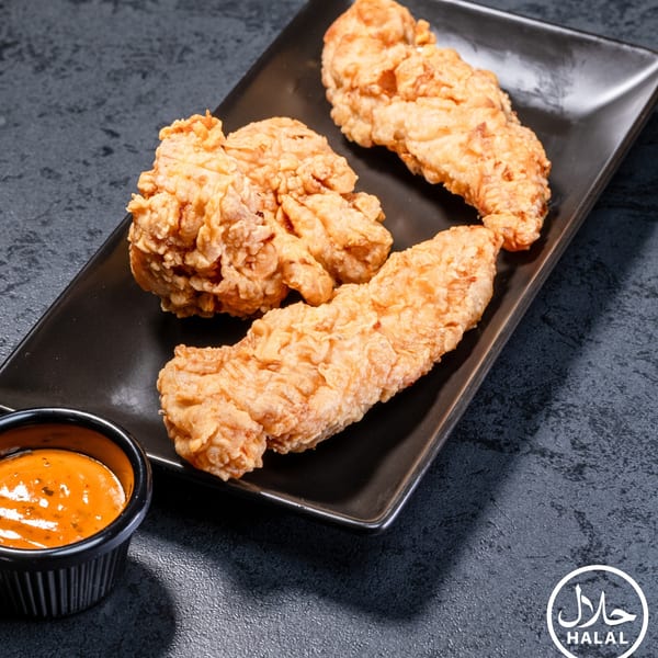Crispy fried chicken tenders on a black rectangular plate with a side of orange dipping sauce.