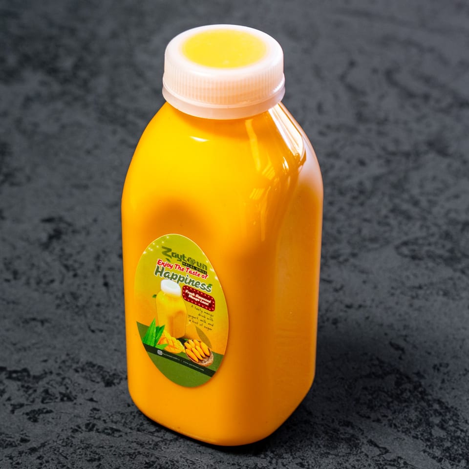 A Zaytun Halal Grill mango lassi bottle with a white cap on a dark gray surface.