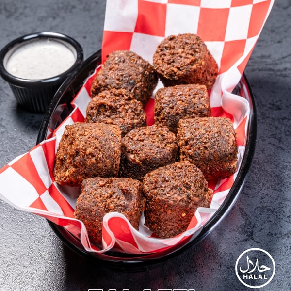 A black basket of crispy, brown falafel pieces with a side of white sauce.