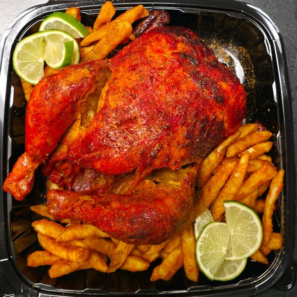 Spicy whole roasted chicken with crispy fries and lime wedges in a black takeout container.