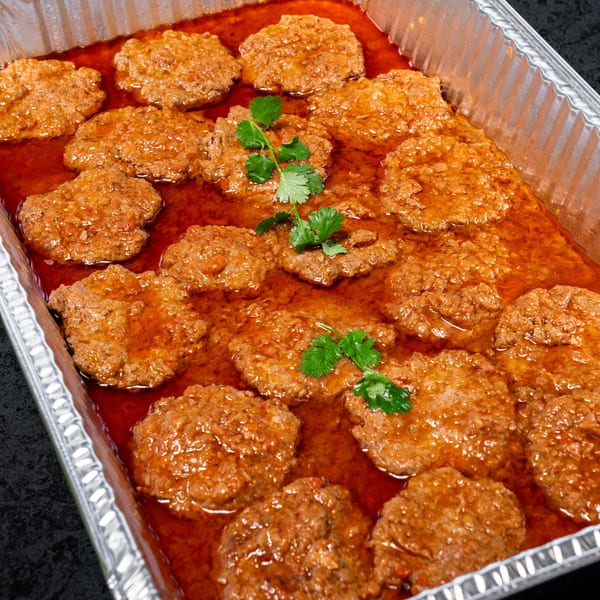 Meat patties in a rich red sauce, garnished with fresh cilantro, in a foil pan.
